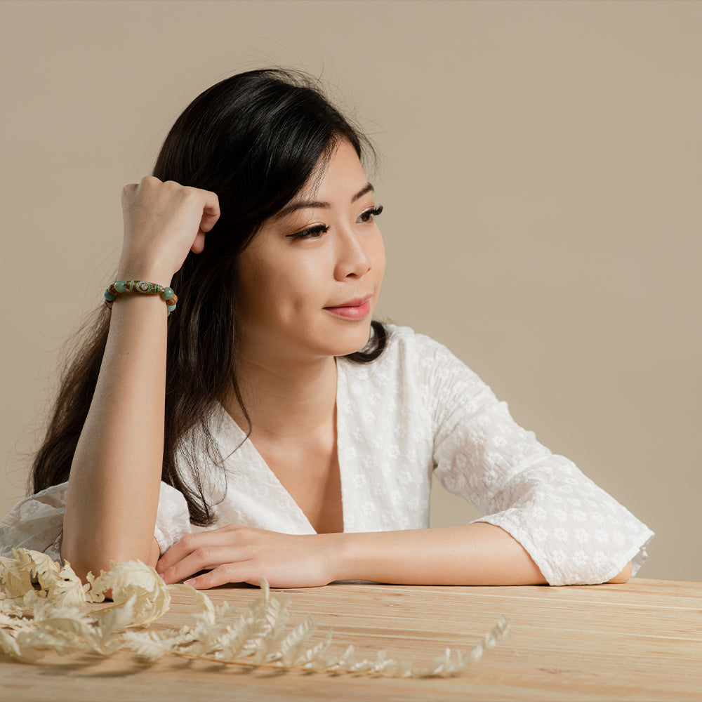 A woman sitting at a table wearing a Pixiu bracelet.